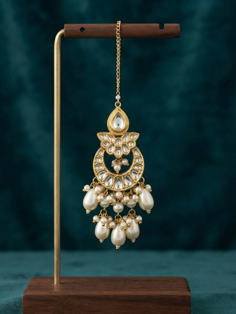 Shop this elegant Kundan maang tikka featuring a chandbali-style pendant, faux pearl drops, and gold-plated detailing. Perfect for weddings, engagements, and festive occasions.
