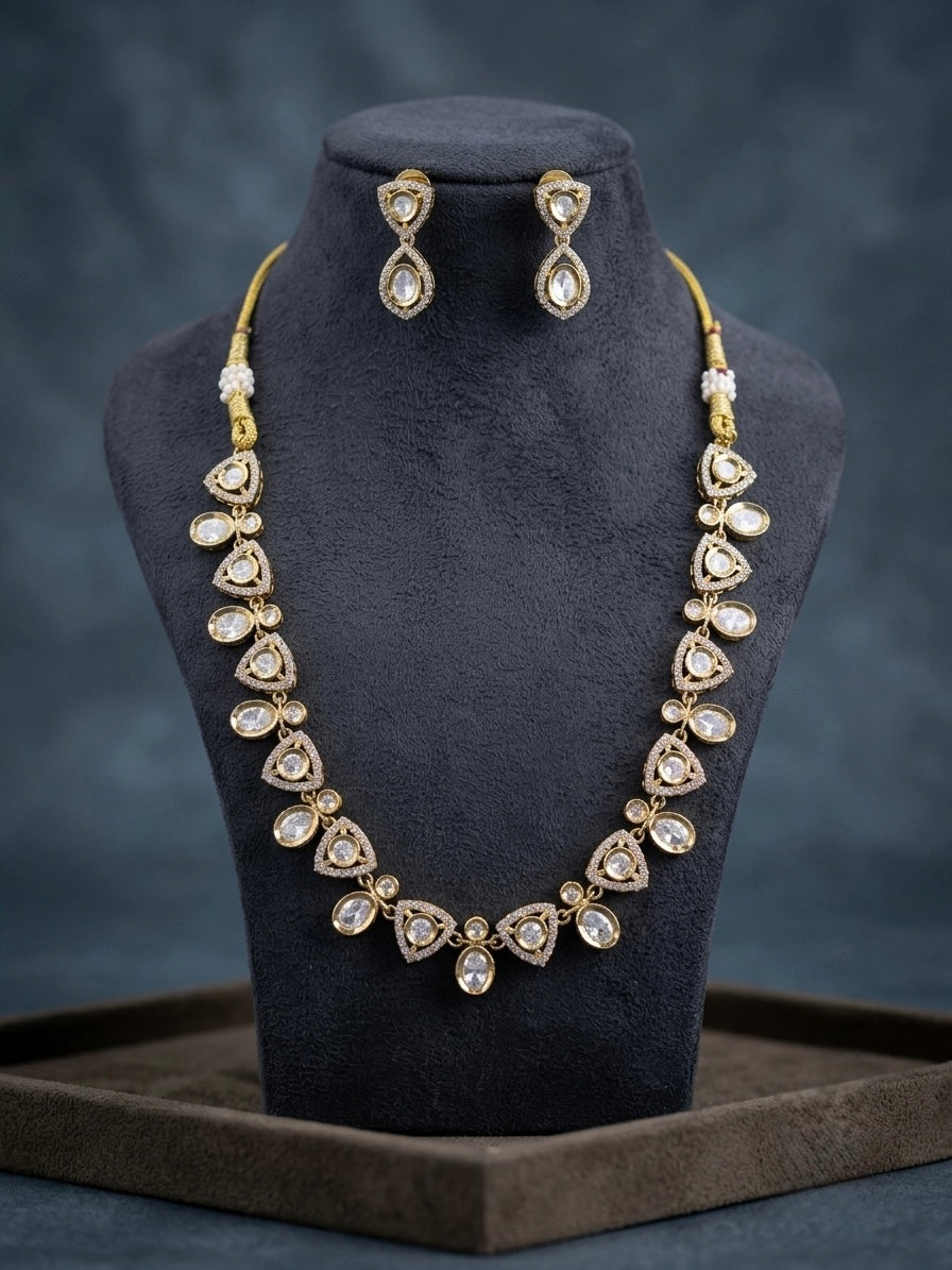 Gold-tone Polki Kundan necklace set with triangle-shaped CZ stone motifs and matching teardrop drop earrings displayed on a black velvet jewelry bust