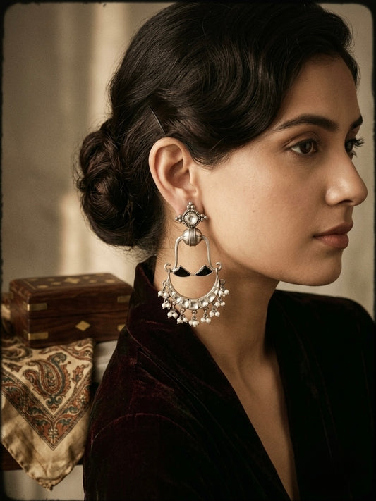 Oxidised 92.5 sterling silver crescent chandelier earrings featuring kundan mirror inlay, black onyx triangular accents, and delicate pearl drop fringe, styled on a model with an elegant updo against a vintage backdrop.